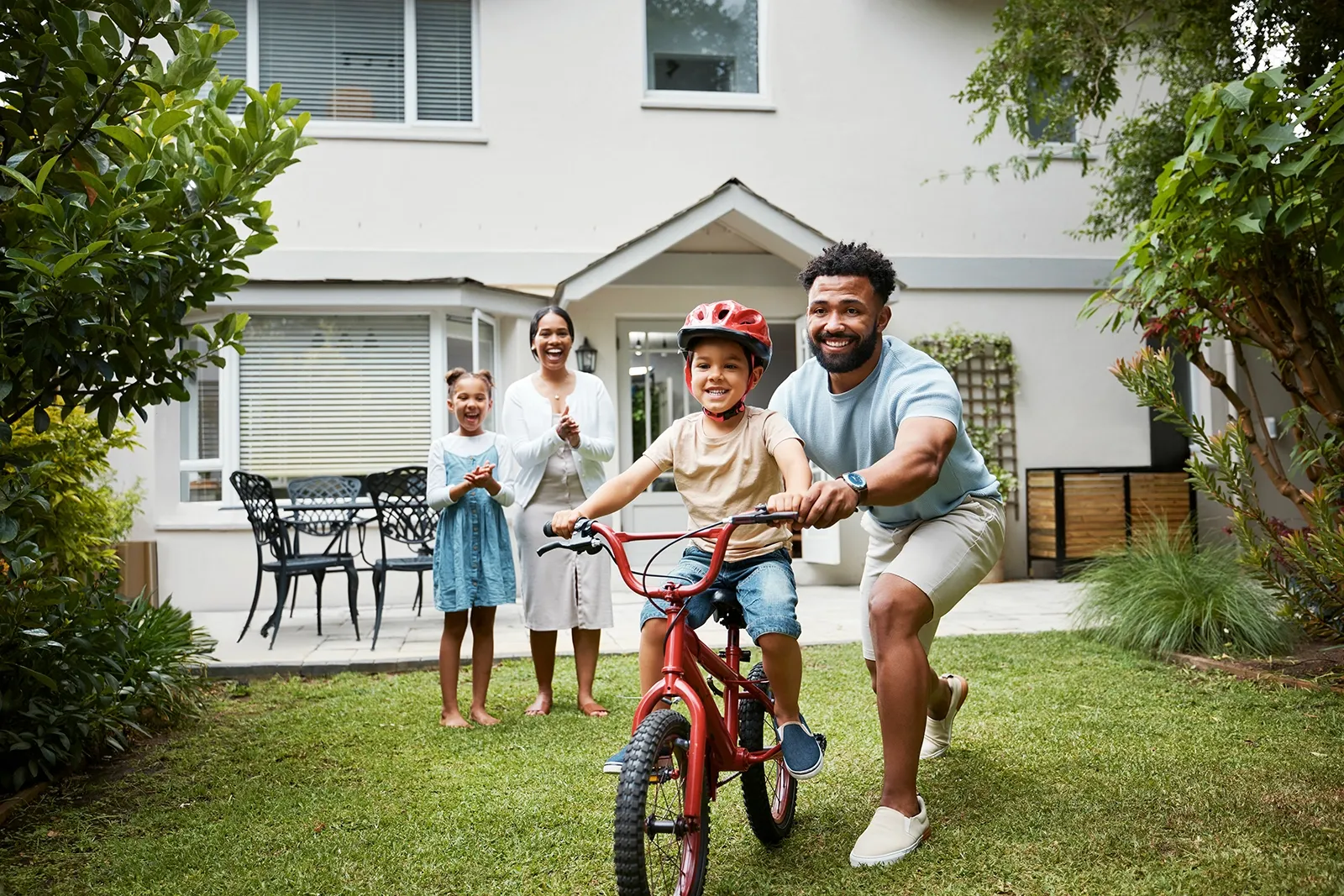 A man pushing his son on a bicycle while his wife stands behind them both